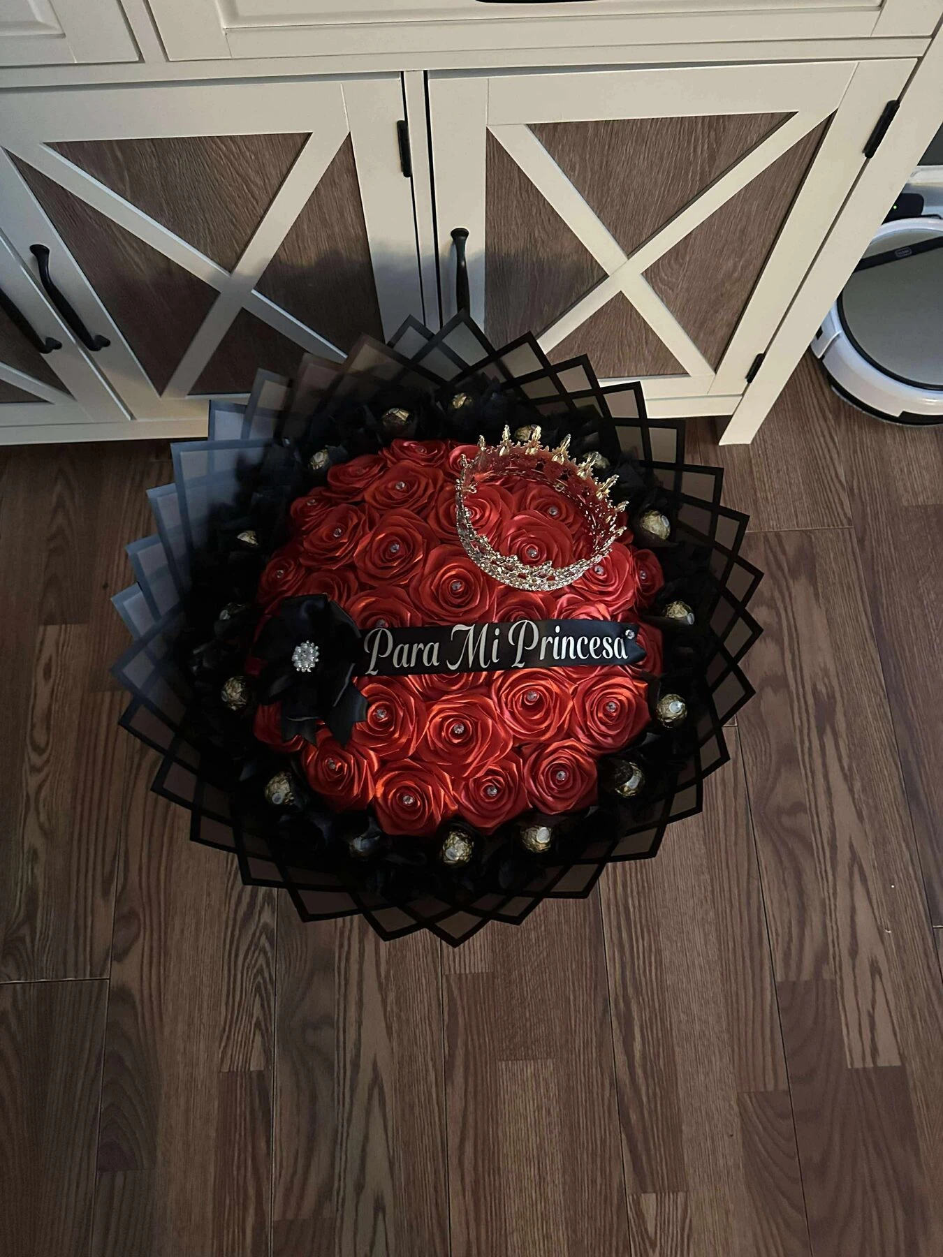 Arreglo floral rojo con envoltura oscura en capas y una cinta clara.