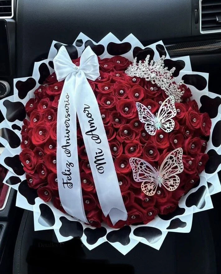 Arreglo floral rojo con cintas claras, adornos de mariposas y envoltura oscura.