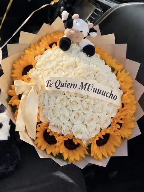 Girasoles y flores claras alrededor de una vaca de peluche, con una cinta en el centro.