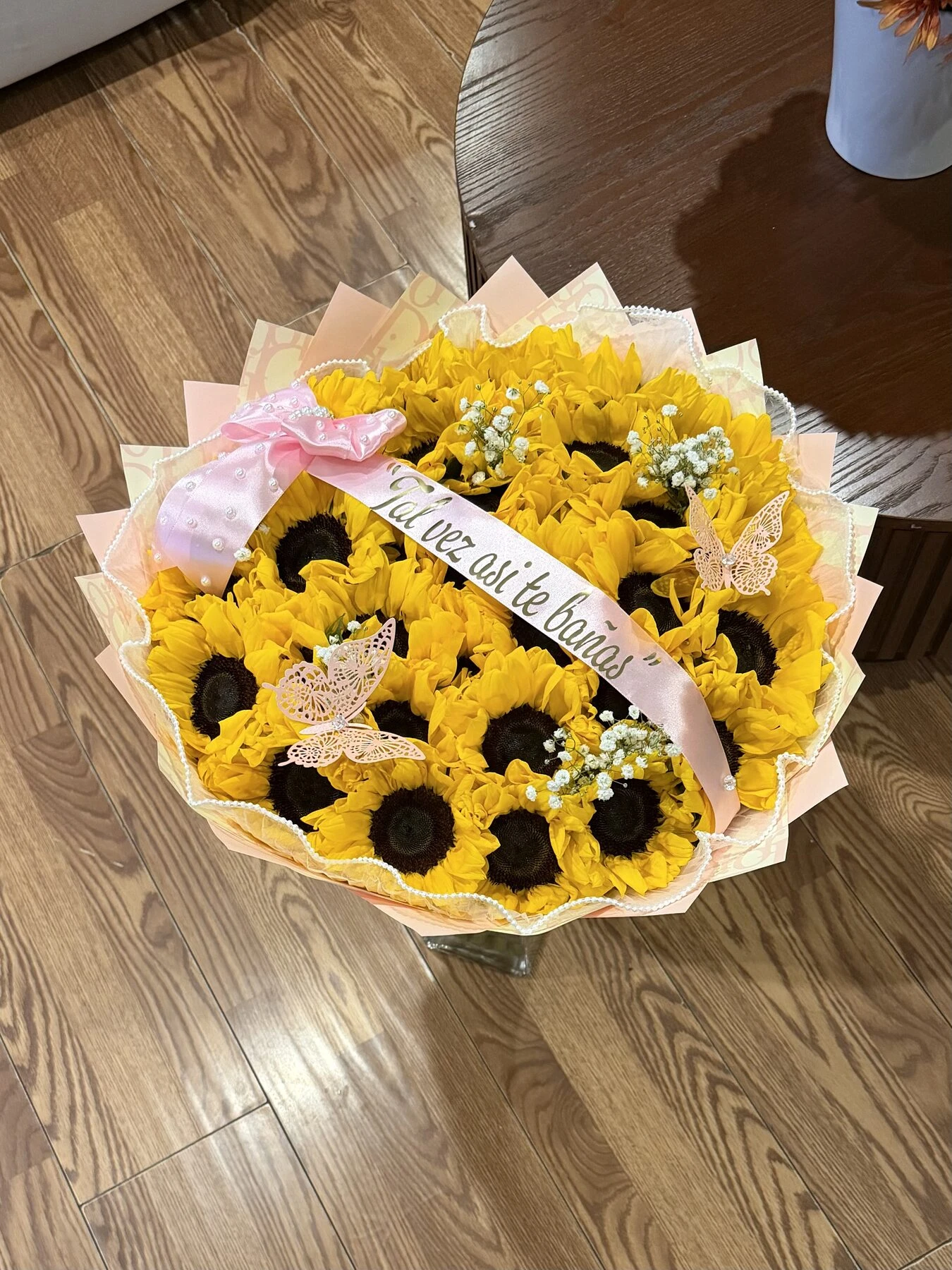 Arreglo floral amarillo y blanco con girasoles, envoltura clara y una cinta.