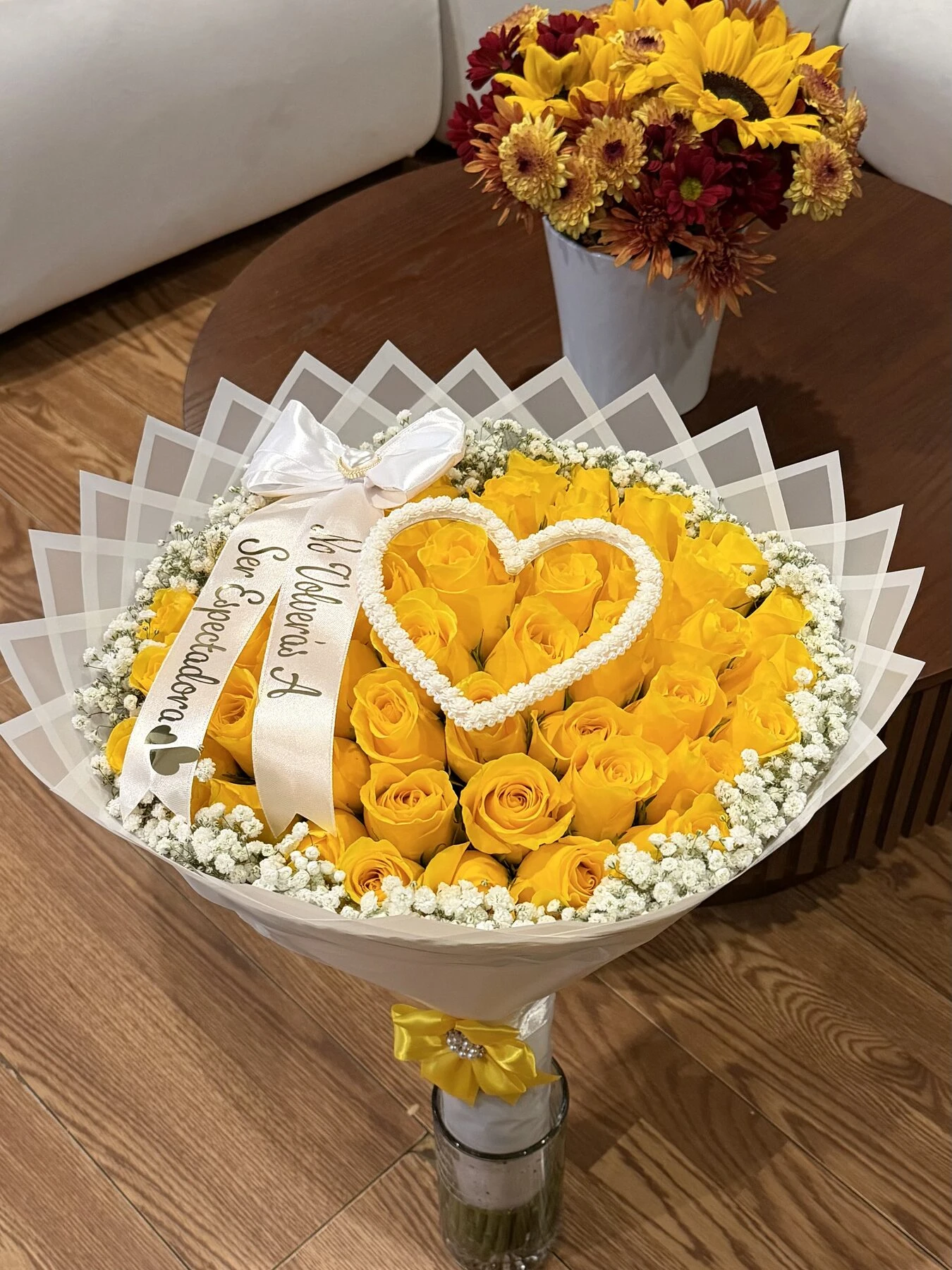 Arreglo floral amarillo con un detalle de corazón blanco, fotografiado desde arriba.
