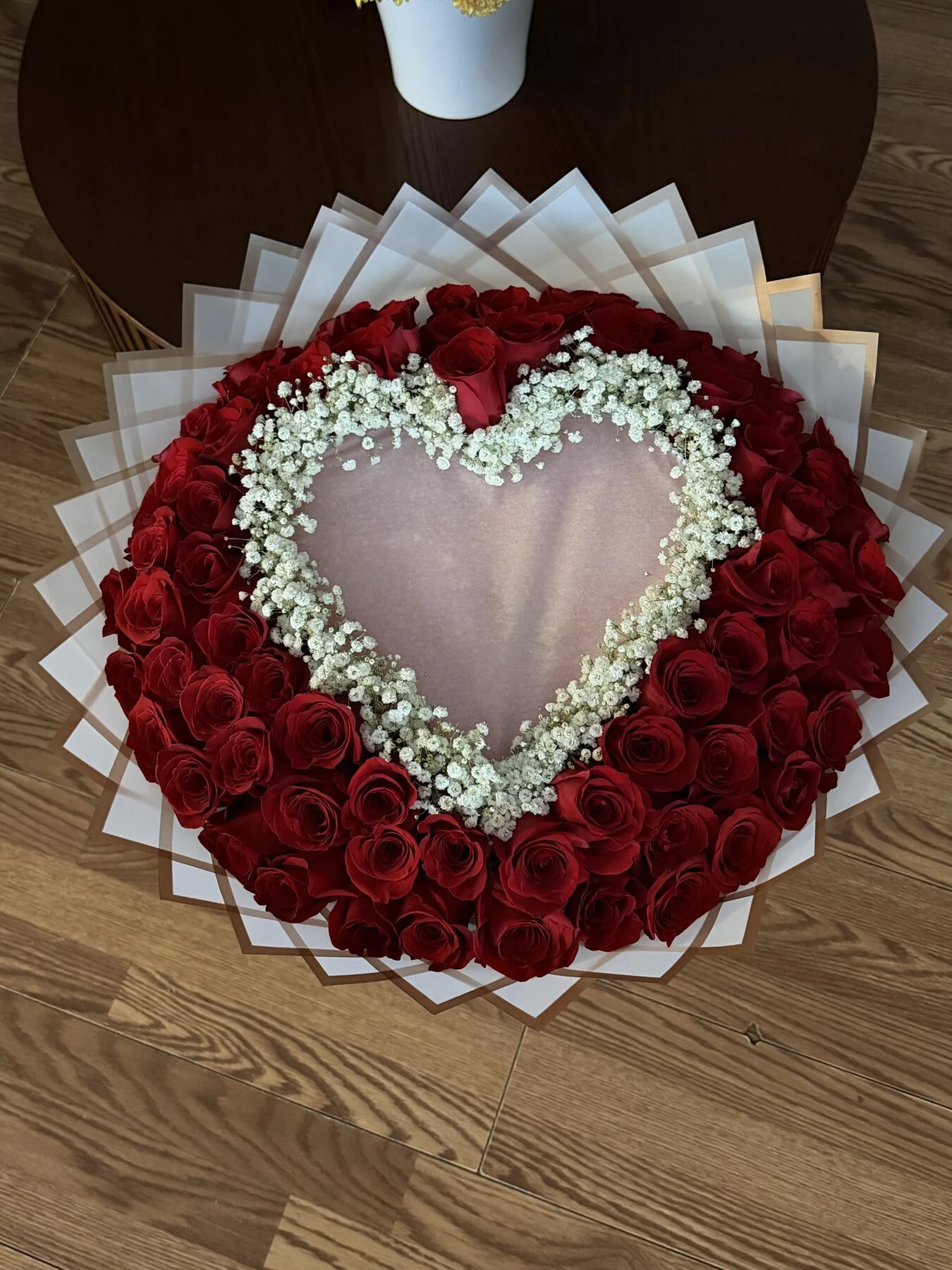 Flores rojas forman un anillo alrededor de un centro claro en forma de corazón, bordeado con flores blancas pequeñas.