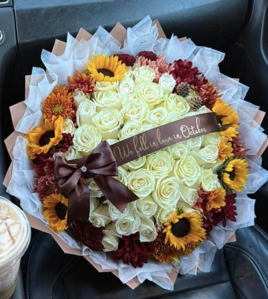 Arreglo abundante de flores color crema con detalles amarillos y naranjas y un lazo oscuro.