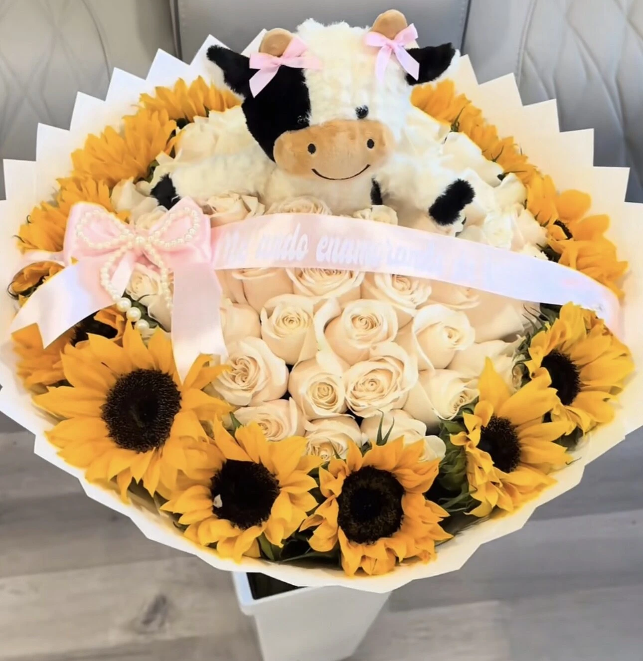 Arreglo floral blanco y amarillo con dos pequeños animales de peluche encima.