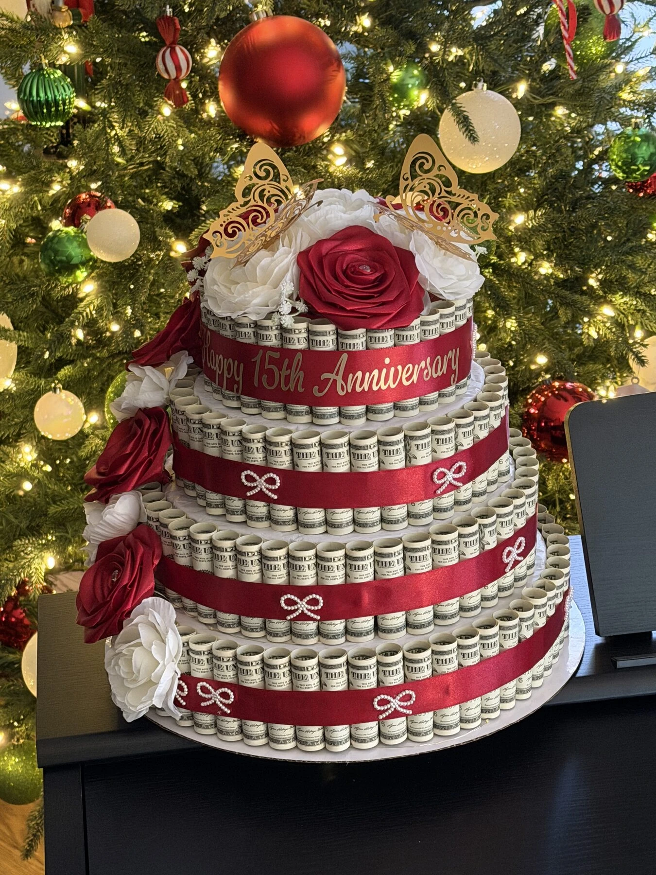 Arreglo en niveles rojo y color crema, fotografiado junto a un árbol decorado.