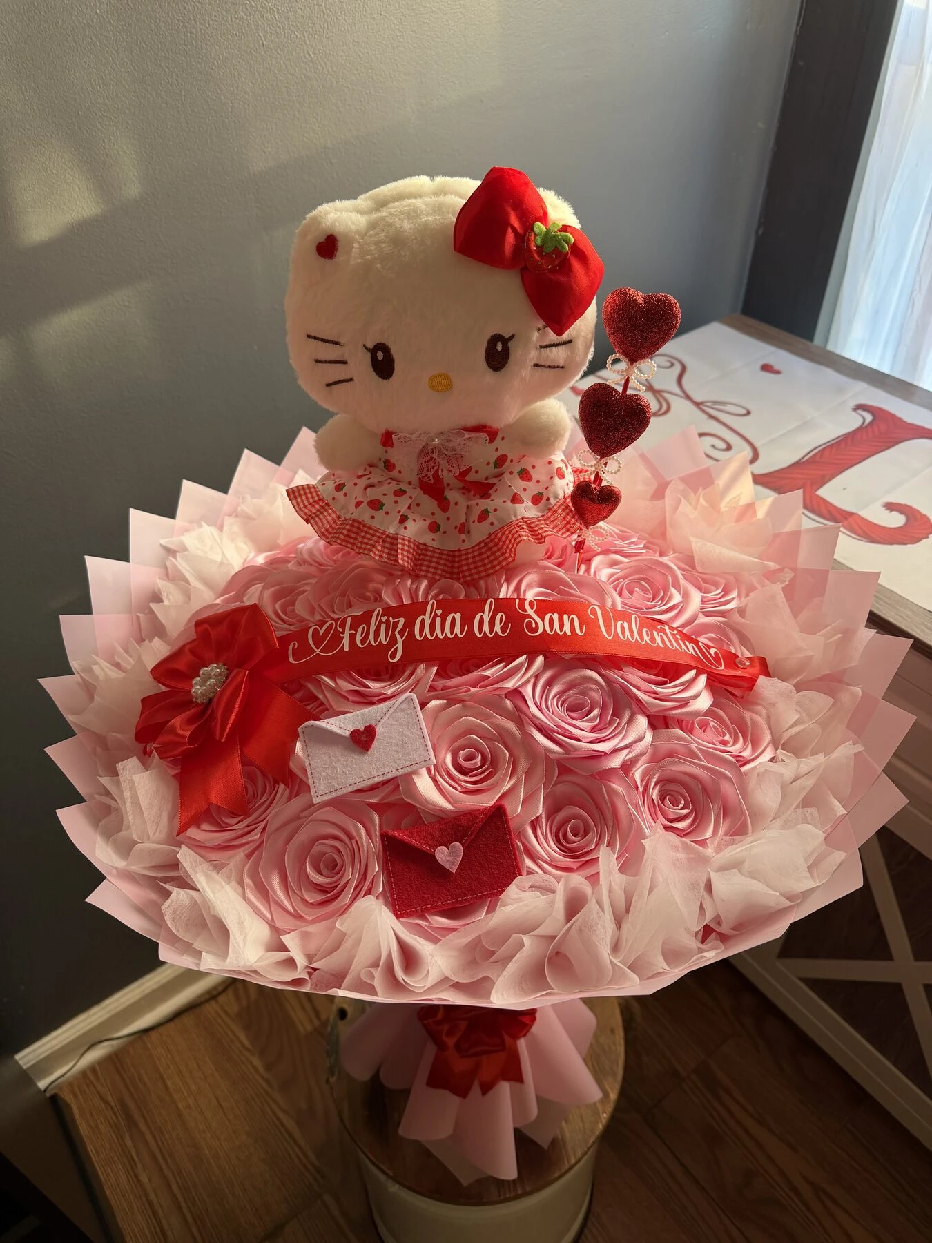 Arreglo floral rosa con un pequeño personaje de peluche y envoltura clara.
