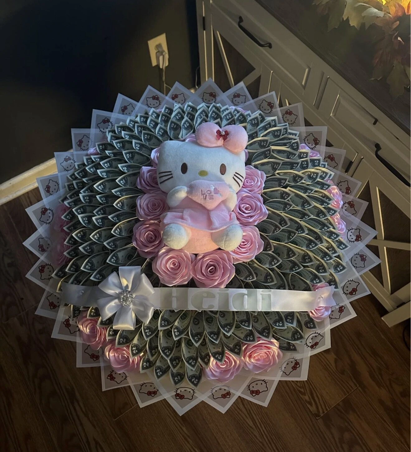 Arreglo redondo de billetes doblados con flores rosas y un pequeño personaje de peluche en el centro.