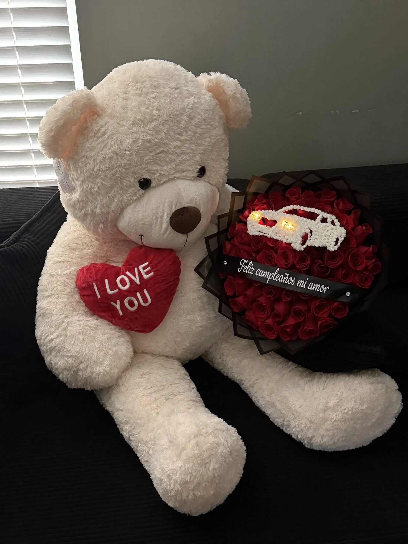 Un oso blanco de peluche junto a un arreglo rojo oscuro con envoltura clara.