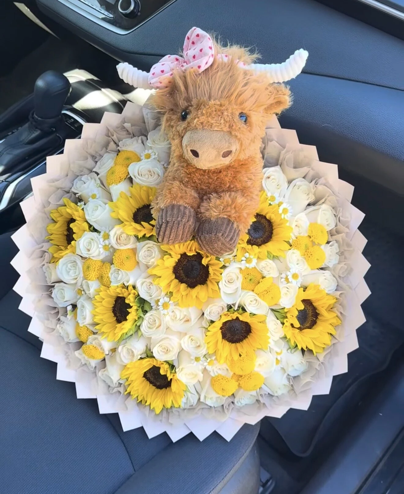 Un pequeño animal de peluche sobre un arreglo de flores amarillas y blancas.