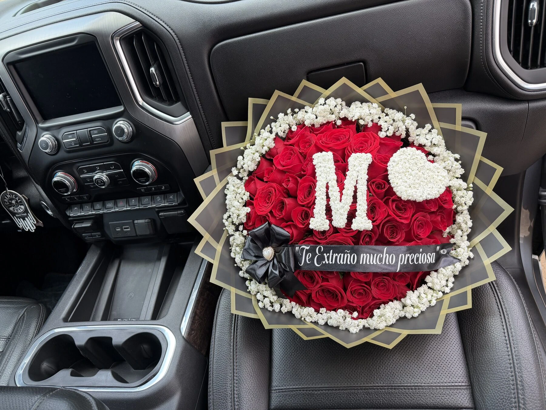 Arreglo floral rojo con una letra clara en el centro, fotografiado dentro de un auto.