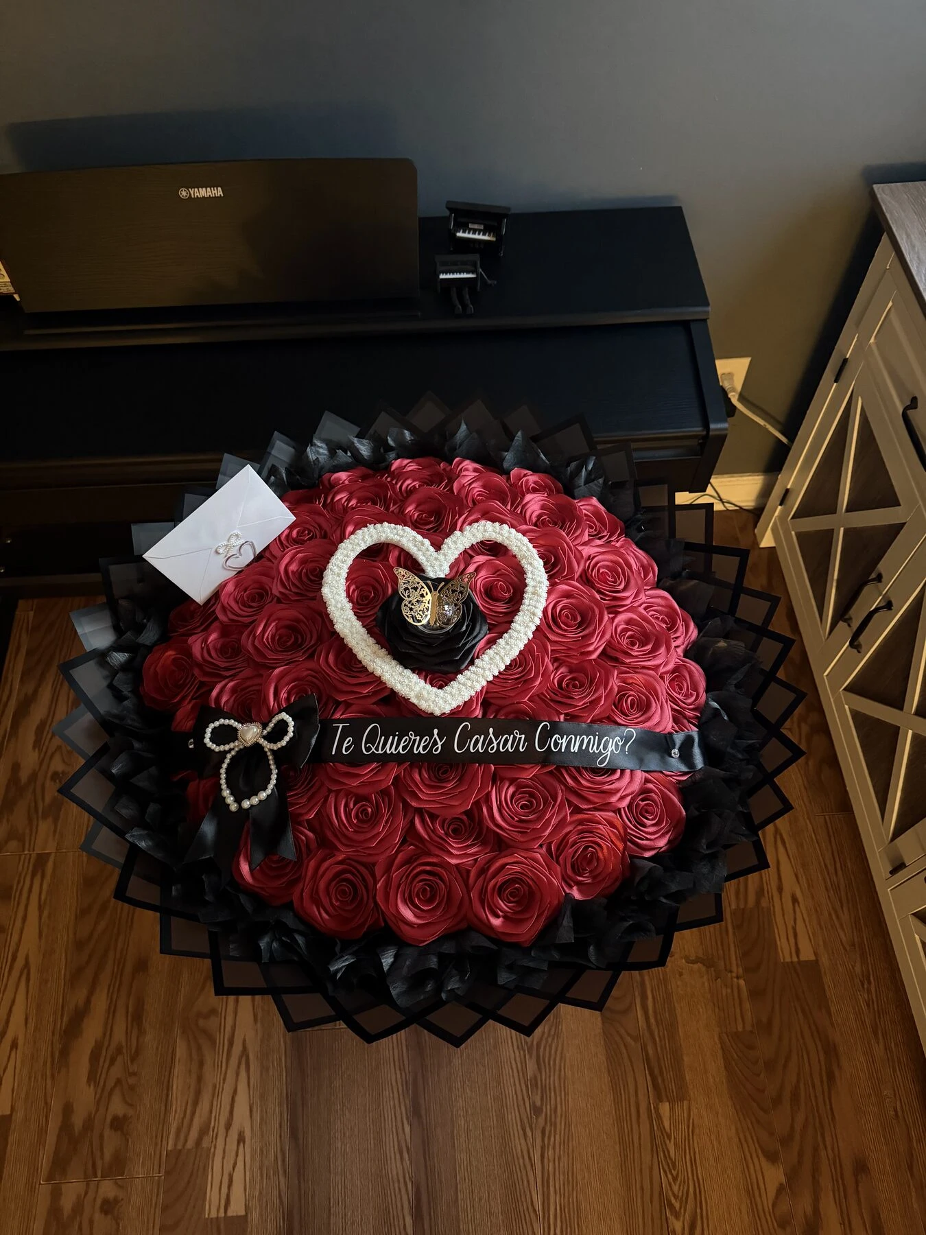 Arreglo floral rojo oscuro con un detalle de corazón y pequeños adornos.