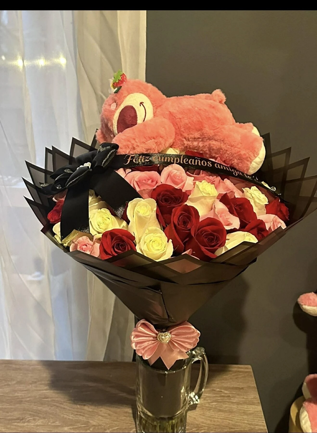 Un oso de peluche rosa sobre un ramo de flores rojas, blancas y rosas.