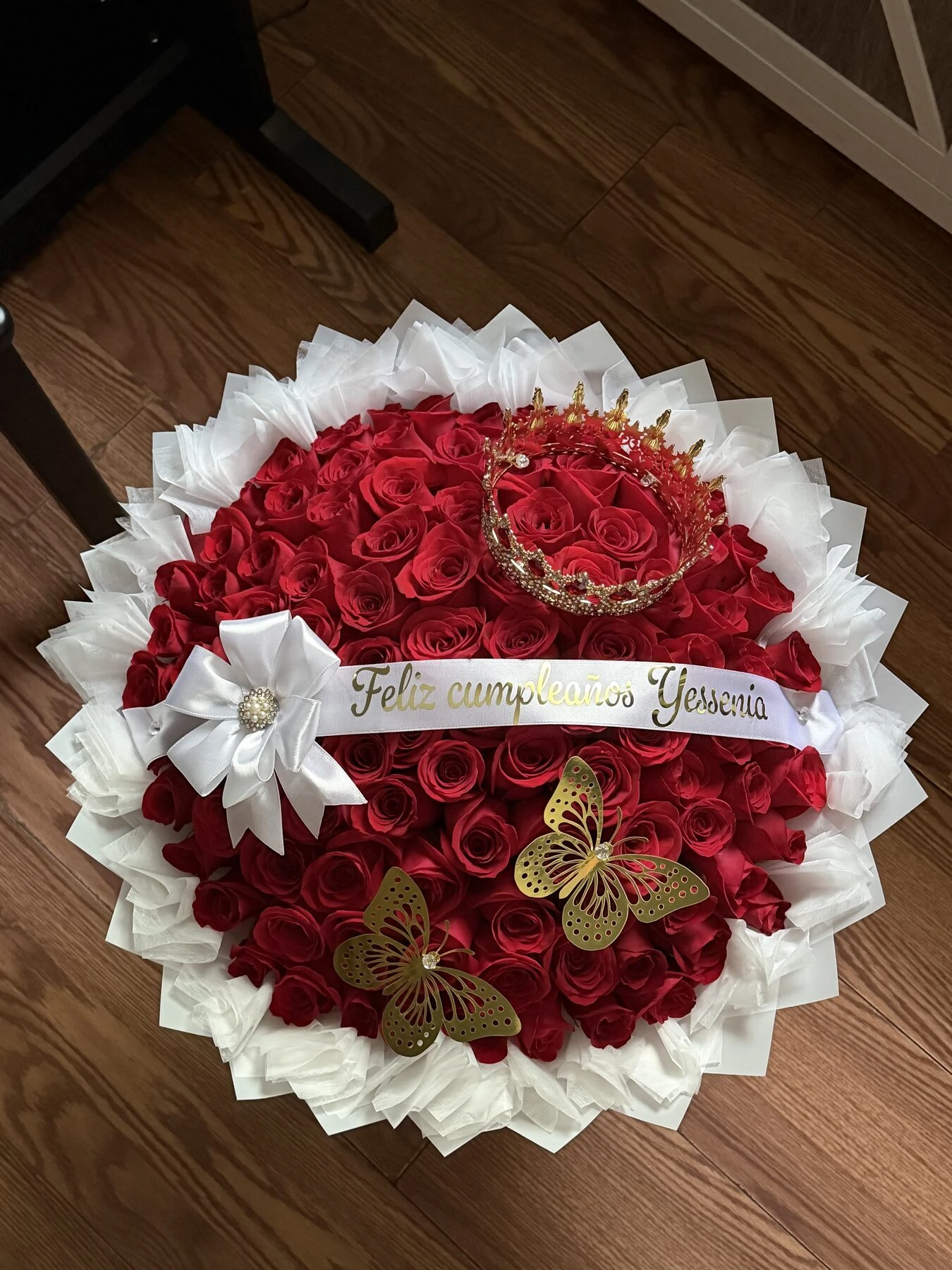 Arreglo floral rojo redondo con envoltura clara, flores blancas pequeñas y detalles decorativos.