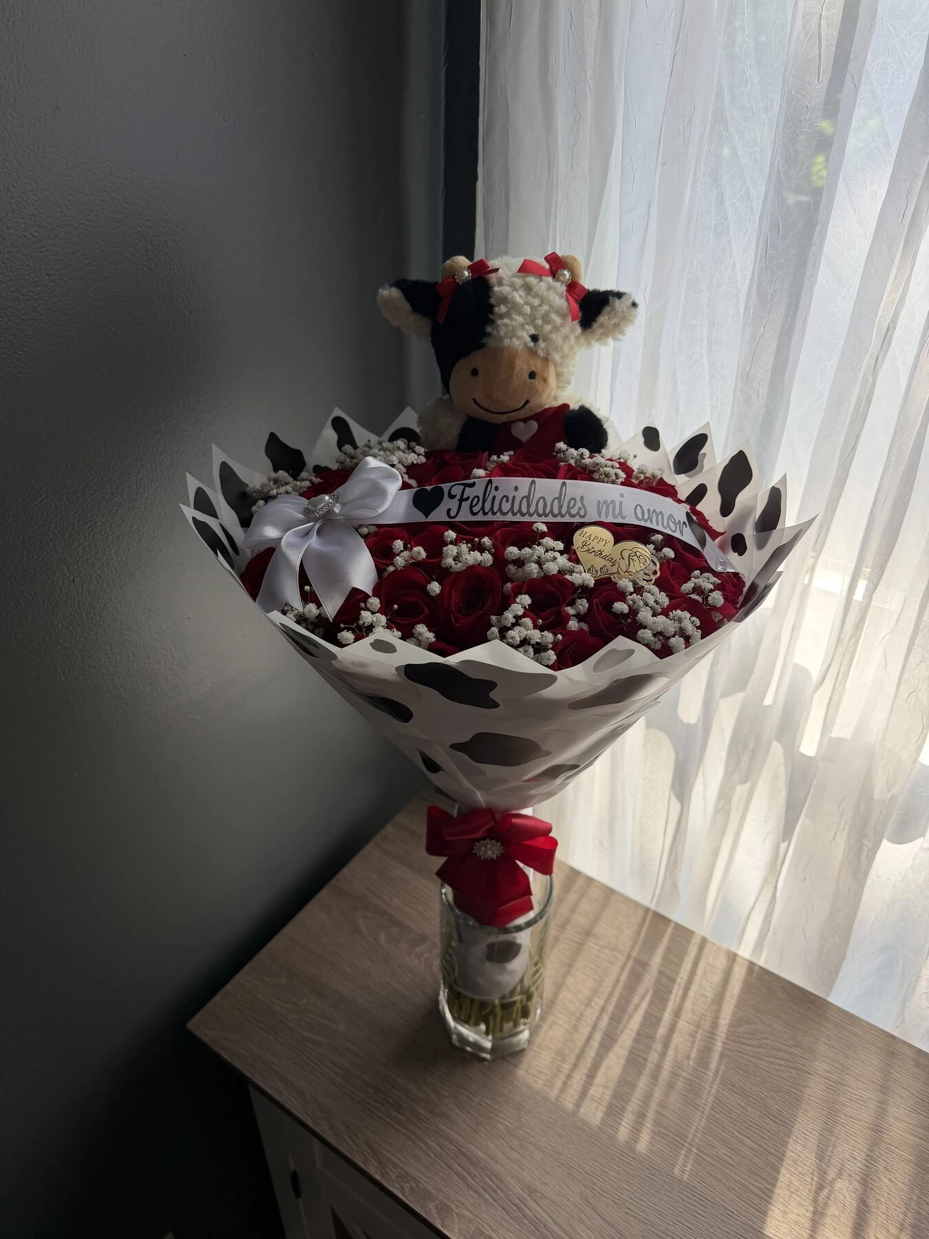 Pequeño arreglo rojo y blanco con una vaca de peluche sobre las flores.