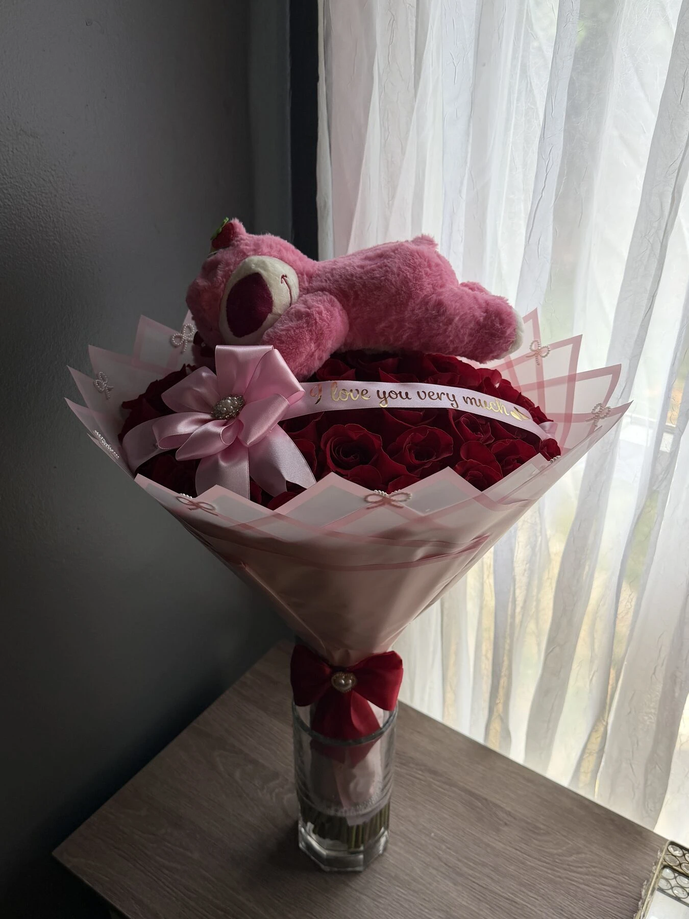 Arreglo rosa y rojo en un florero con un pequeño peluche en el centro.